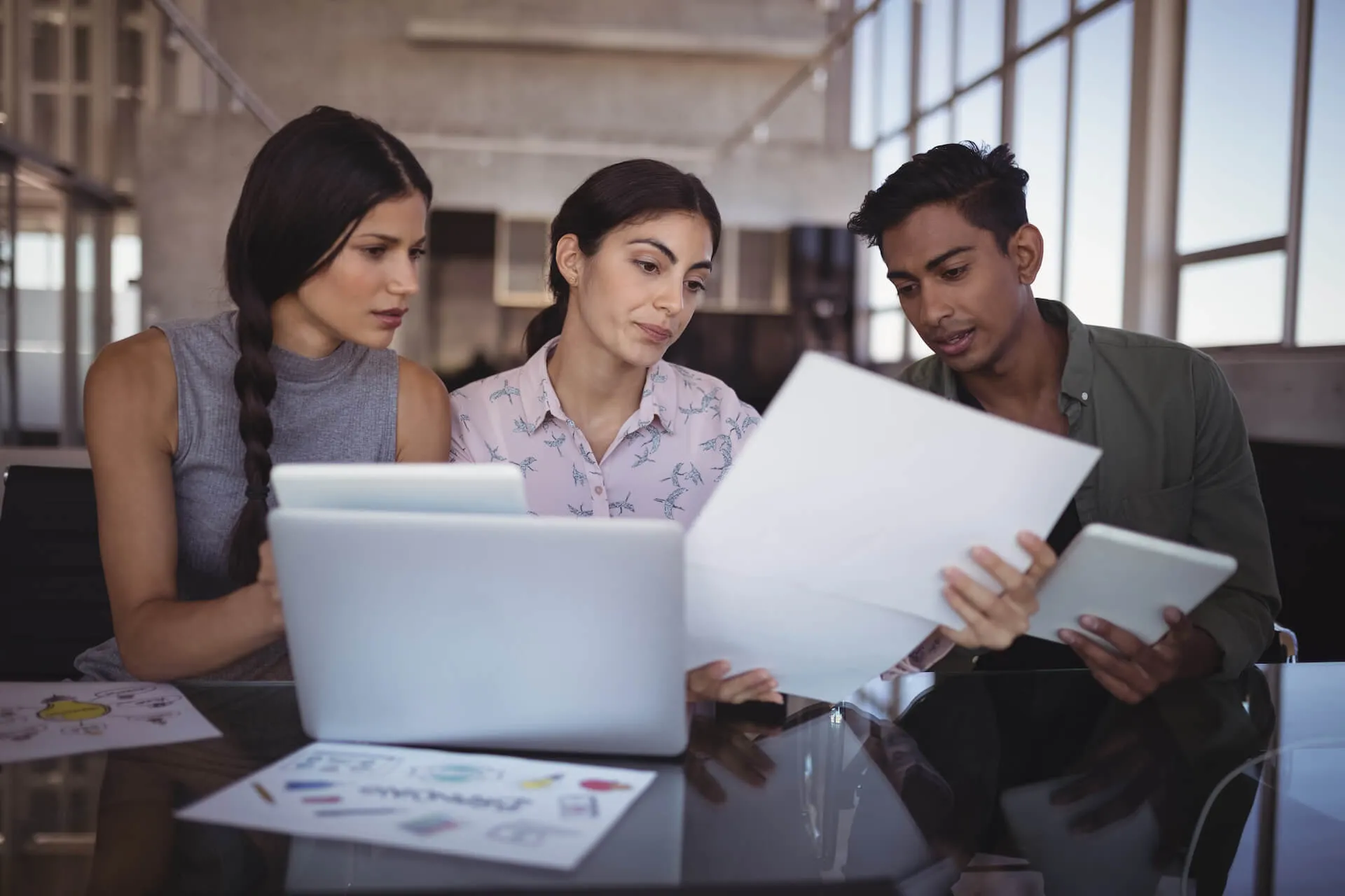 Group of six diverse colleagues leaning over a table reviewing colorful charts and graphs during a collaborative meeting.